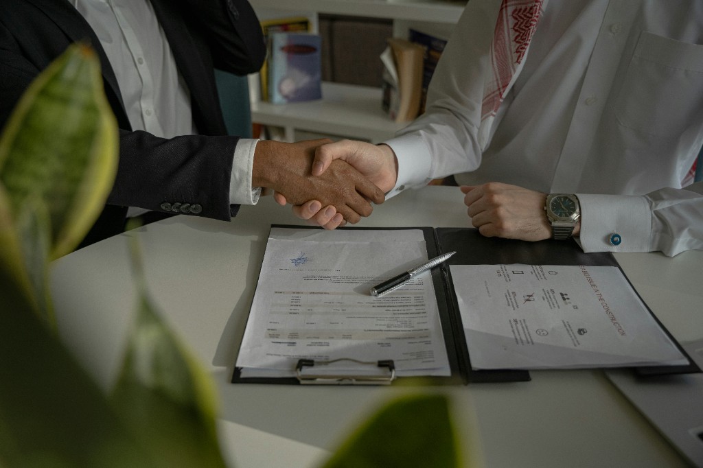 Two professionals shaking hands over contract documents